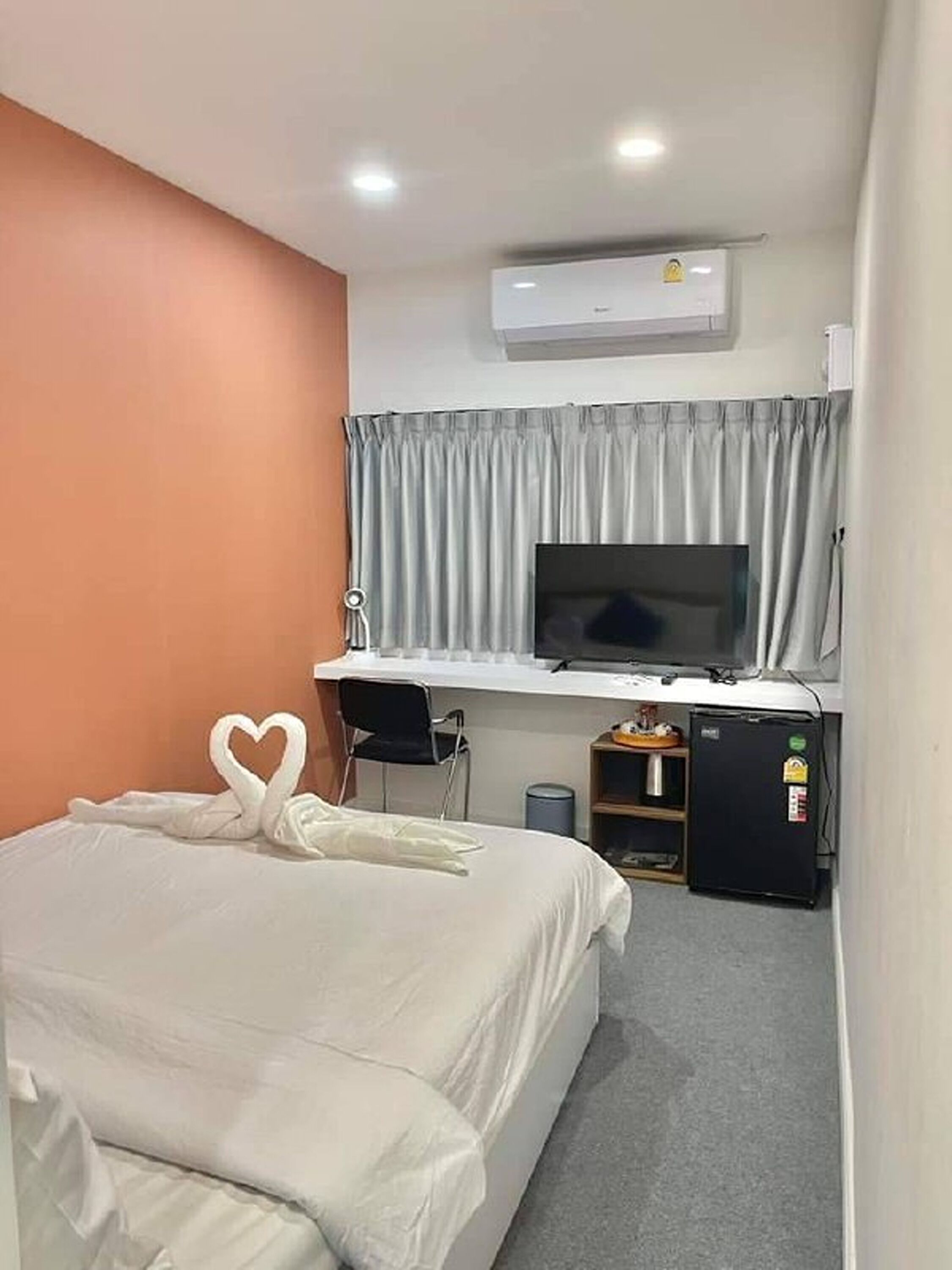A hotel room with a bed, a desk with a computer, a TV, and a mini-fridge.