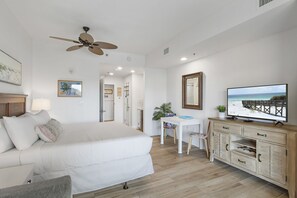 Un dormitorio con una cama, un escritorio, un televisor y un ventilador de techo.