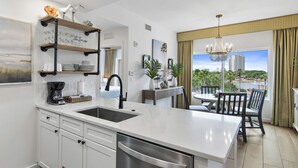 A modern kitchen with a large island, white cabinetry, and a view of a balcony with a dining area. - Pool View ~ Oversized Balcony ~ Tram Included (Miramar Beach)