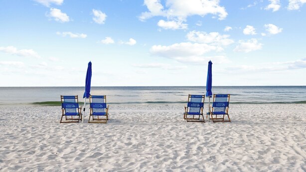 A beach with four blue lounge chairs and matching umbrellas, arranged in a row facing the ocean. - White Caps 503 by Liquid Life (Orange Beach)