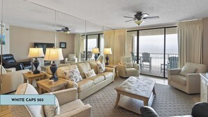 A spacious living room with a sofa, armchairs, a coffee table, and lamps. There are ceiling fans, a large window with curtains, and a view of the outdoors. - White Caps 503 by Liquid Life (Orange Beach)