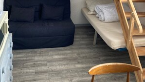 Una habitación pequeña con una cama litera, un sofá y una silla de madera.