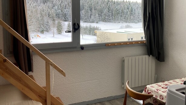 Una habitación con una escalera de madera, una mesa con mantel estampado y vistas a un bosque nevado a través de una ventana.