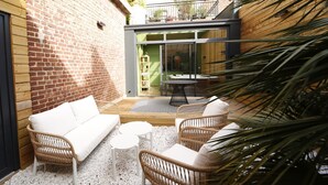 A cozy outdoor seating area with wicker furniture and a small round table, surrounded by a brick wall and a wooden deck. - L Arbre d or Appart Hyper Centre SPA Couvert (Cambrai)