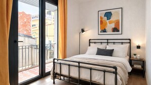 A bedroom with a bed, a nightstand, a lamp, a window with curtains, and a painting on the wall.