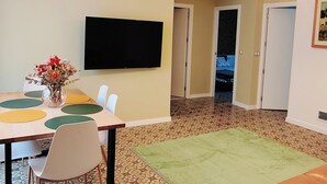 A dining area with a table, chairs, a vase with flowers, a flat-screen TV on the wall, and a patterned floor.