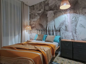Um quarto com cama, mesa de cabeceira, cômoda e parede com textura de pedra.