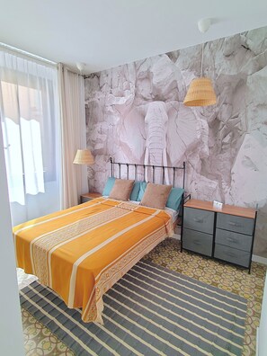 Une chambre à coucher comprenant un lit, des tables de chevet, une commode, un tapis à motifs et un mur en pierre orné d’une sculpture d’éléphant.