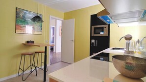 A kitchen with a microwave, sink, and a large bowl on the counter. There are two stools and a painting on the wall.