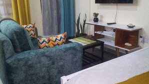 A hotel room with a bed, a sofa, a TV, and a desk. - Lux Suites Vet Studio Apartments (Ngong)