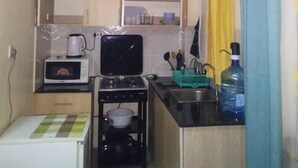 A compact kitchen with a microwave, toaster, and small stove. There is a sink and a water bottle on the counter. - Lux Suites Vet Studio Apartments (Ngong)