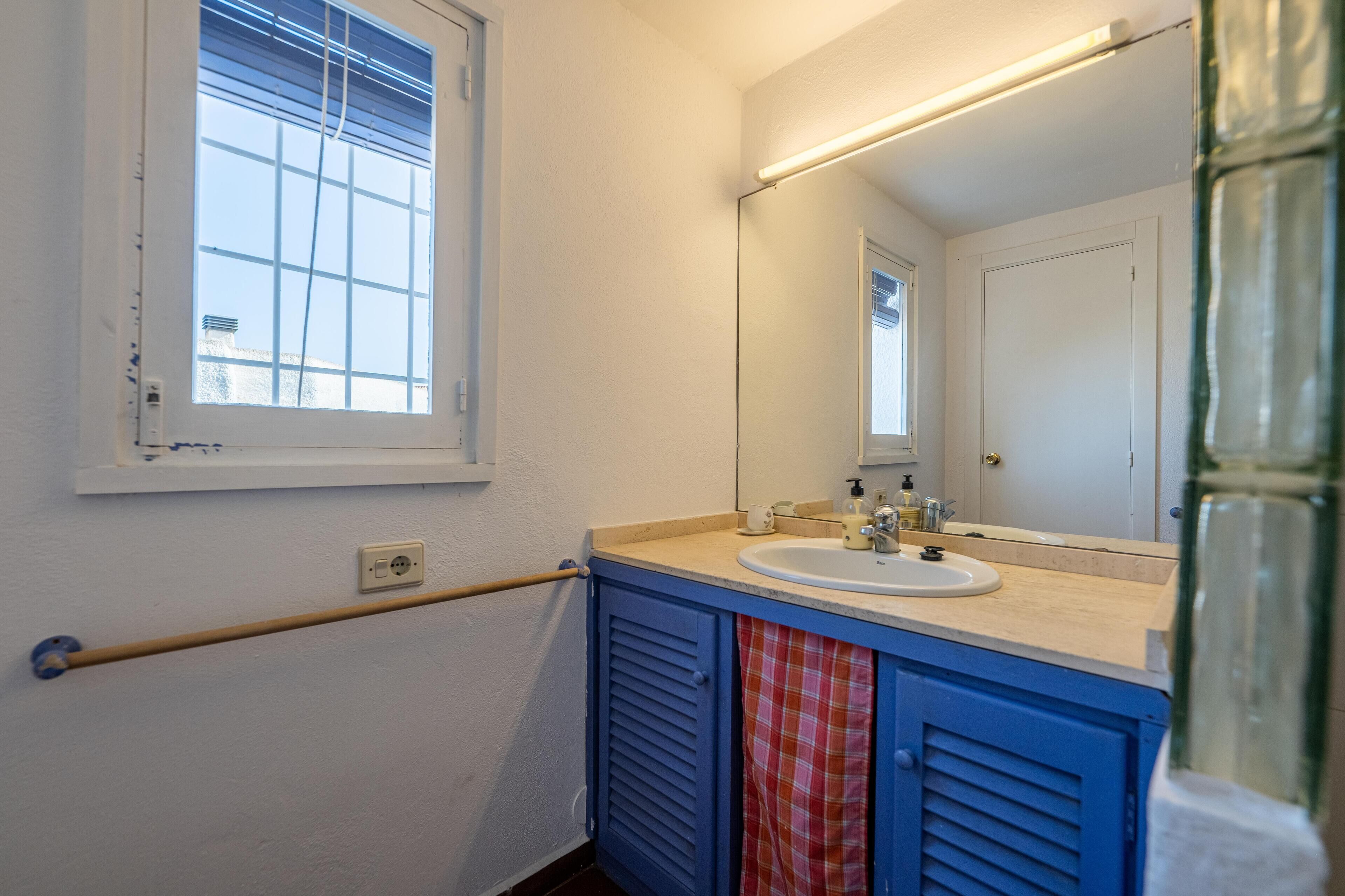 Baño con ventana, lavabo, espejo y perchero para toallas.