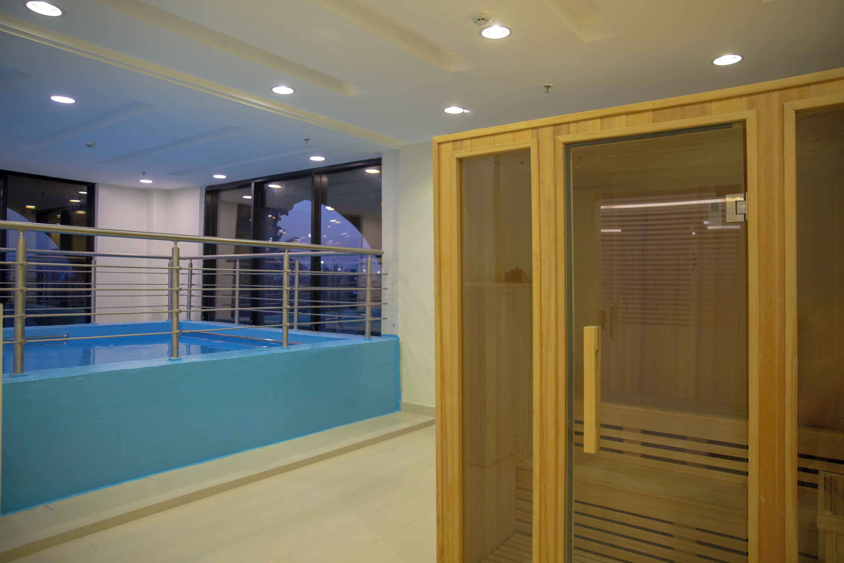 Una piscina interior moderna con zona azulada y puerta de cristal de madera.