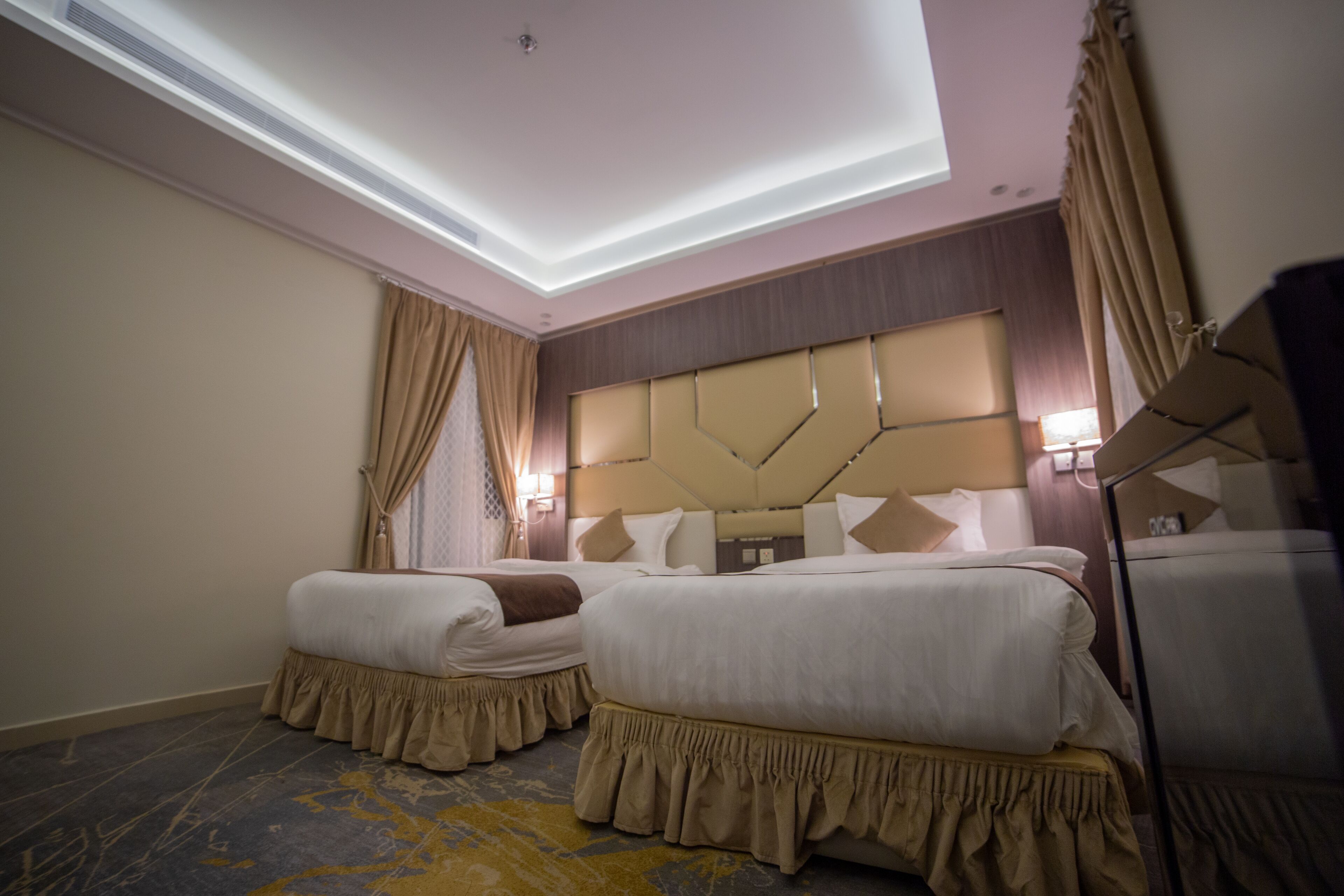 A hotel room with two beds, a large headboard, and a ceiling light.