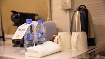 Mostrador de hotel con dos botellas de agua, una toalla, dos tazas blancas, un hervidor y una cafetera.
