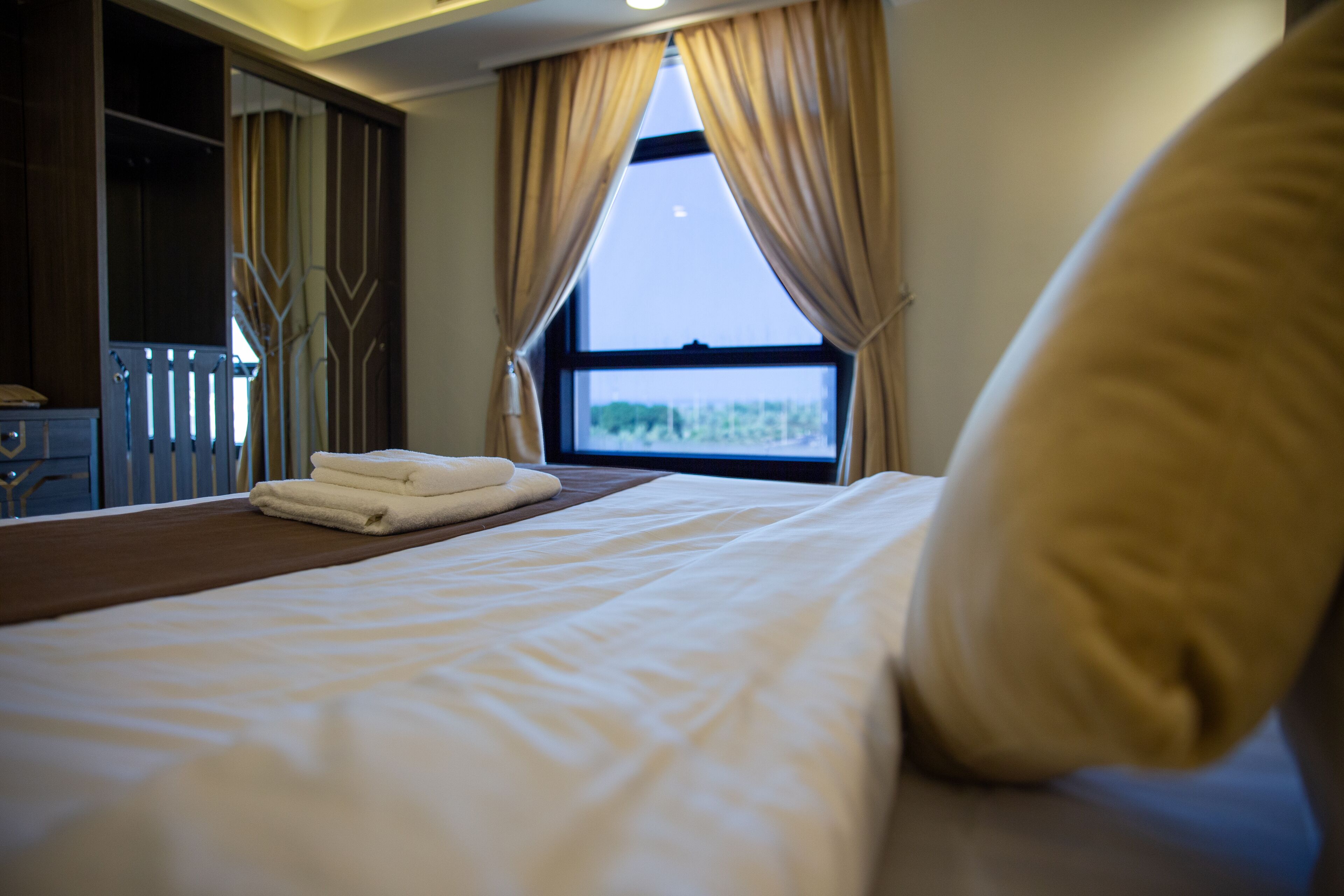 Ein Hotelzimmer mit Bett, einem Fenster mit Vorhängen, einem Nachttisch und einem Kleiderschrank.