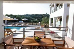 A poolside area with lounge chairs, a wooden table with a fruit bowl, and a view of a pool and hillside. - Michelangelo Suites and Apartments (Parga)
