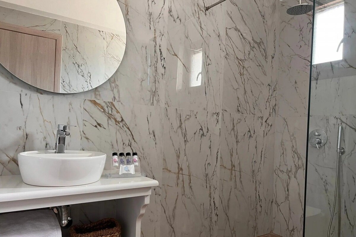 A modern bathroom with a marble vanity, a glass shower enclosure, and a wooden cabinet.