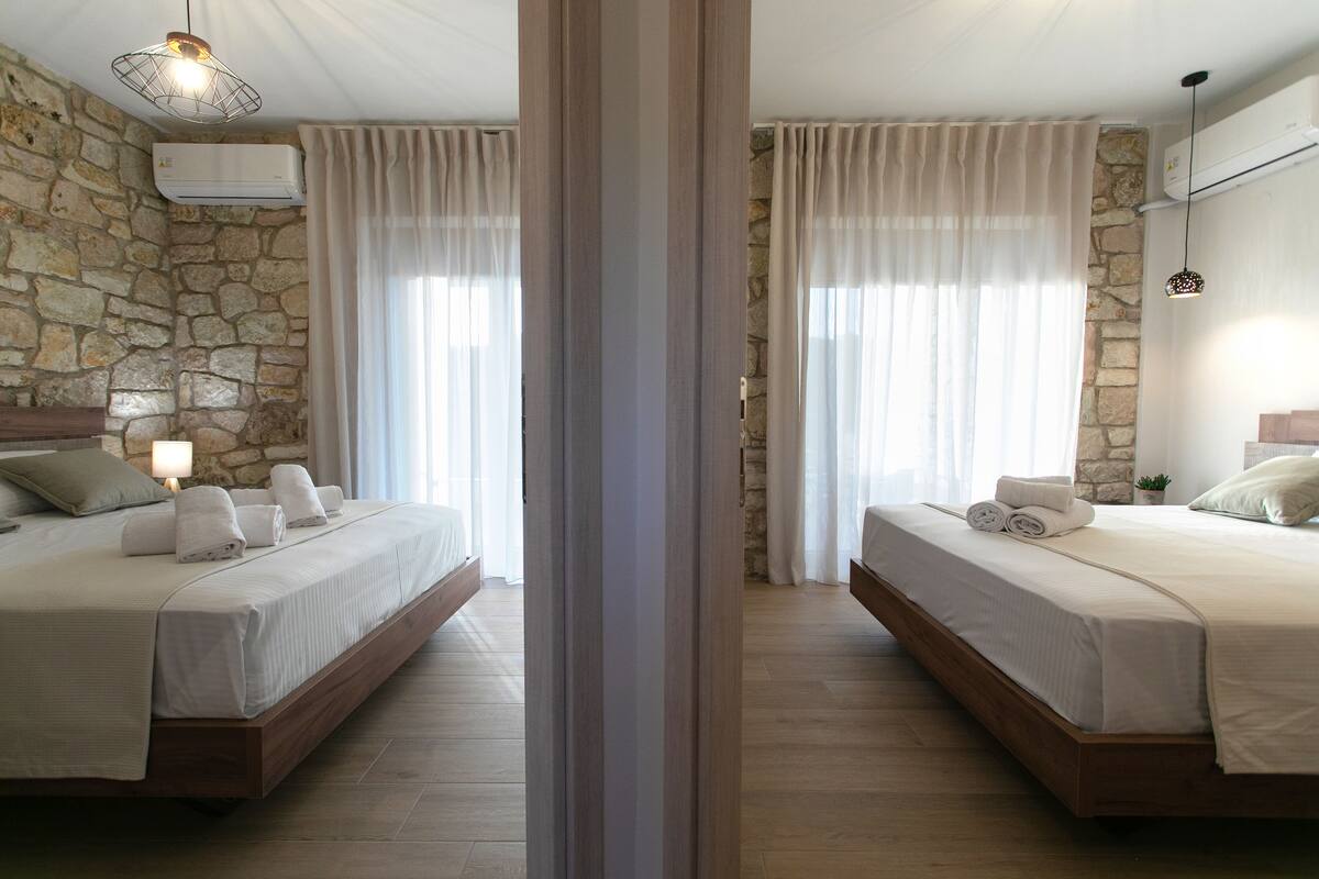 A hotel room with two beds, stone walls, wooden floors, and a modern design.
