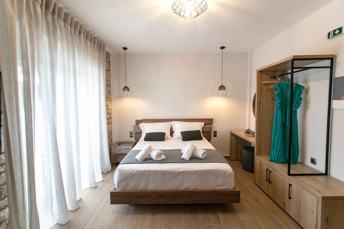 A modern hotel room with a wooden bed, white bedding, a wardrobe, and a mirror.