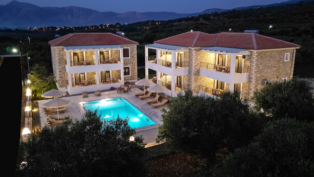 A two-story stone building with a swimming pool, outdoor seating, and a view of mountains. - Michelangelo Suites and Apartments (Parga)