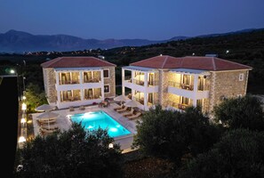 A two-story stone building with a swimming pool, outdoor seating, and a view of mountains. - Michelangelo Suites and Apartments (Parga)