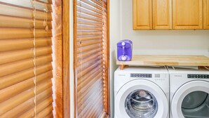 A laundry area with two white front-loading washing machines, wooden cabinets, and a window with blinds. - Secluded Catskill Home w/ Hiking Trails On-site! (Catskill)