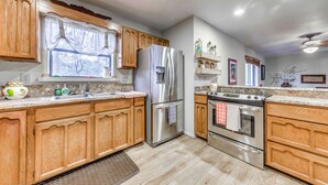 A kitchen with wooden cabinets, stainless steel appliances, a window with curtains, and a tiled floor. - Expansive Ruidoso Home: Private Hot Tub + Deck (Ruidoso)