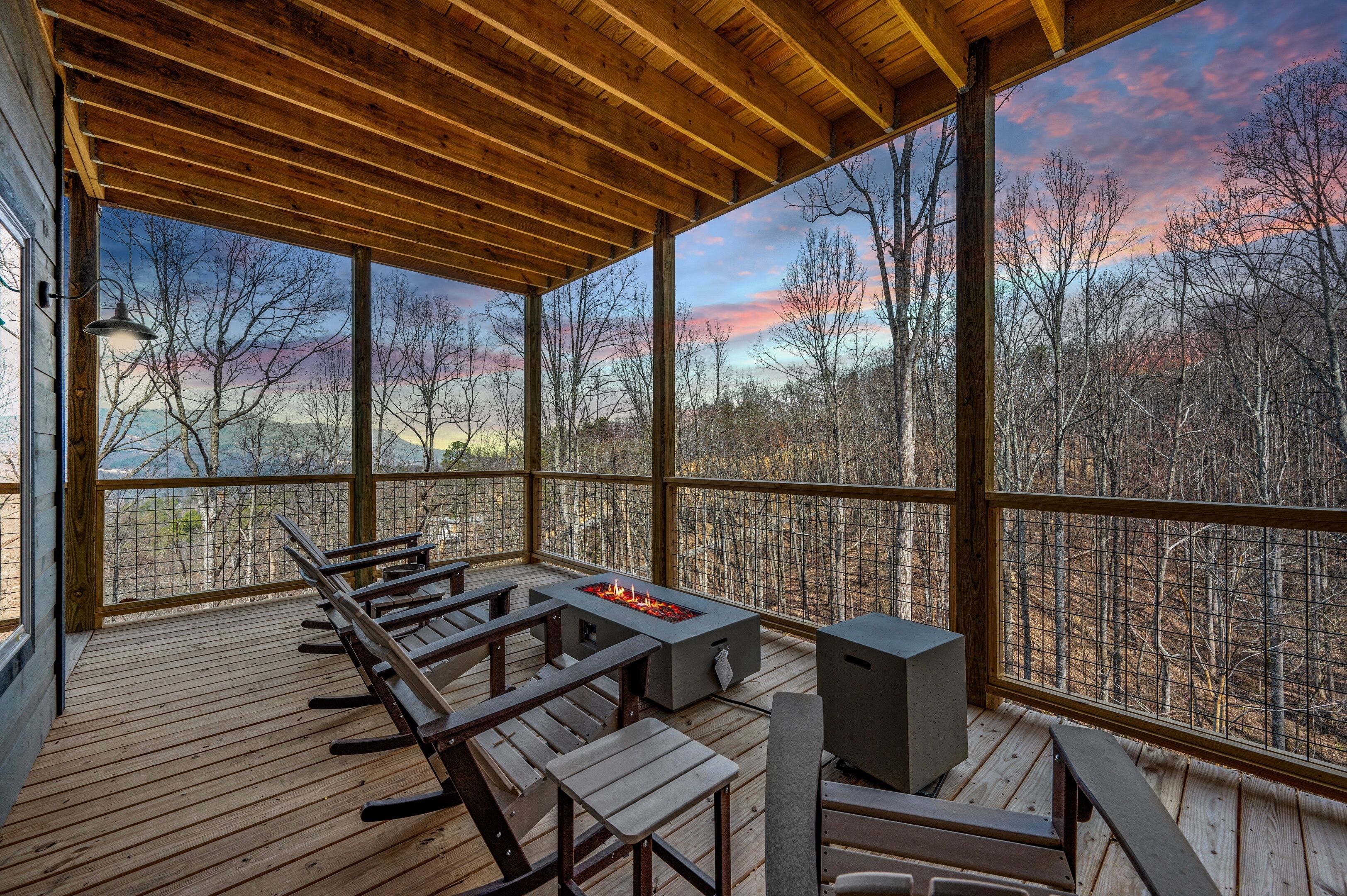 A covered deck with wooden benches and a fire pit, overlooking a forested area.