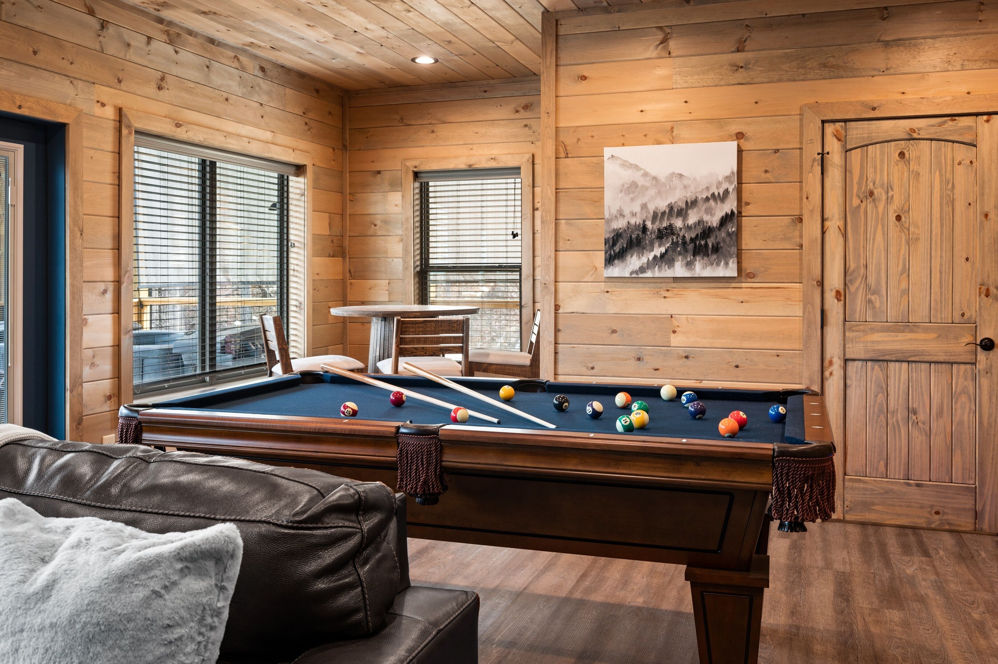 A pool table in a wooden room with a couch and a painting on the wall.