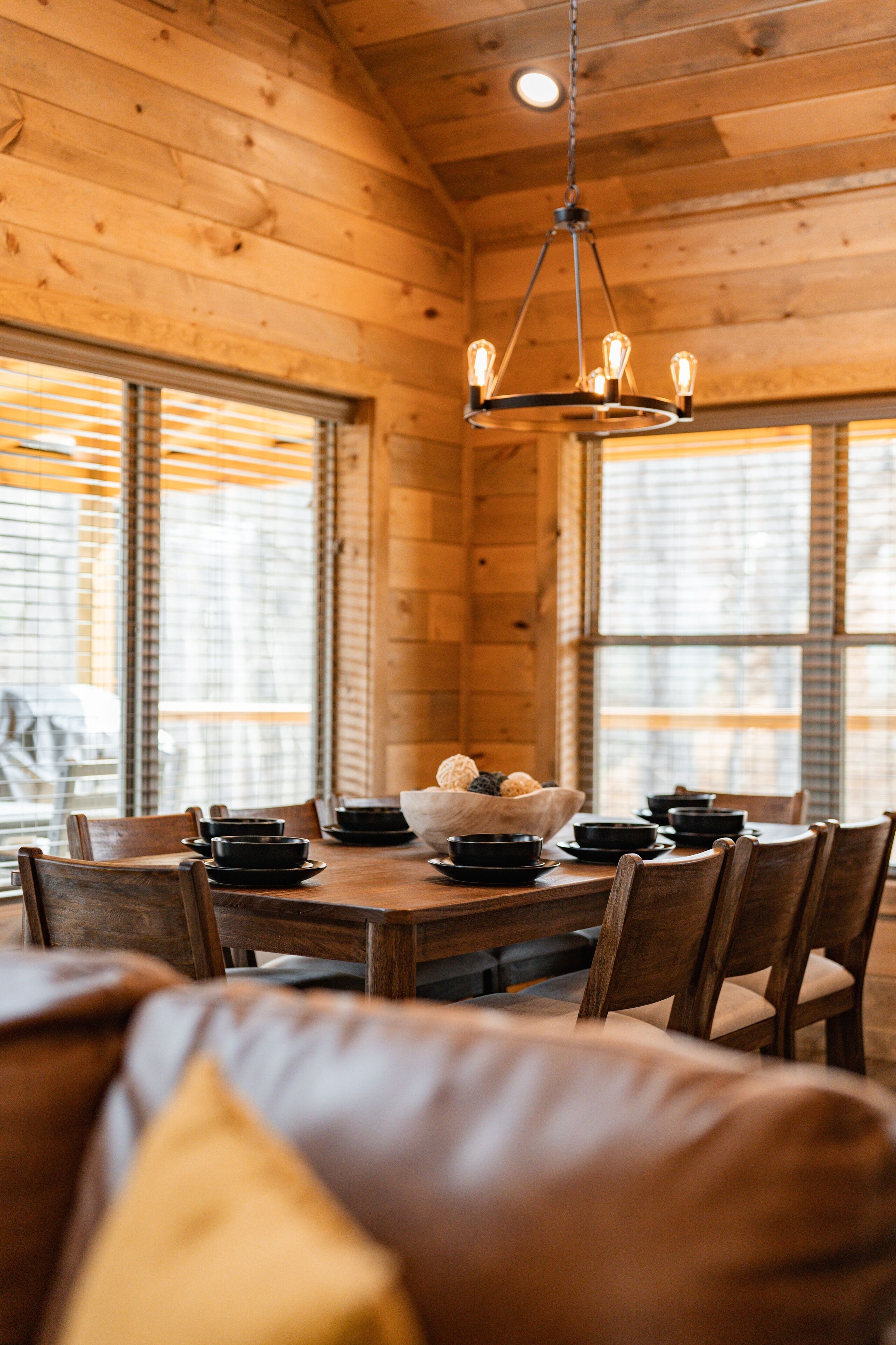 Een houten interieur met een eettafel gedekt voor vier personen, omringd door stoelen, en een kroonluchter erboven.
