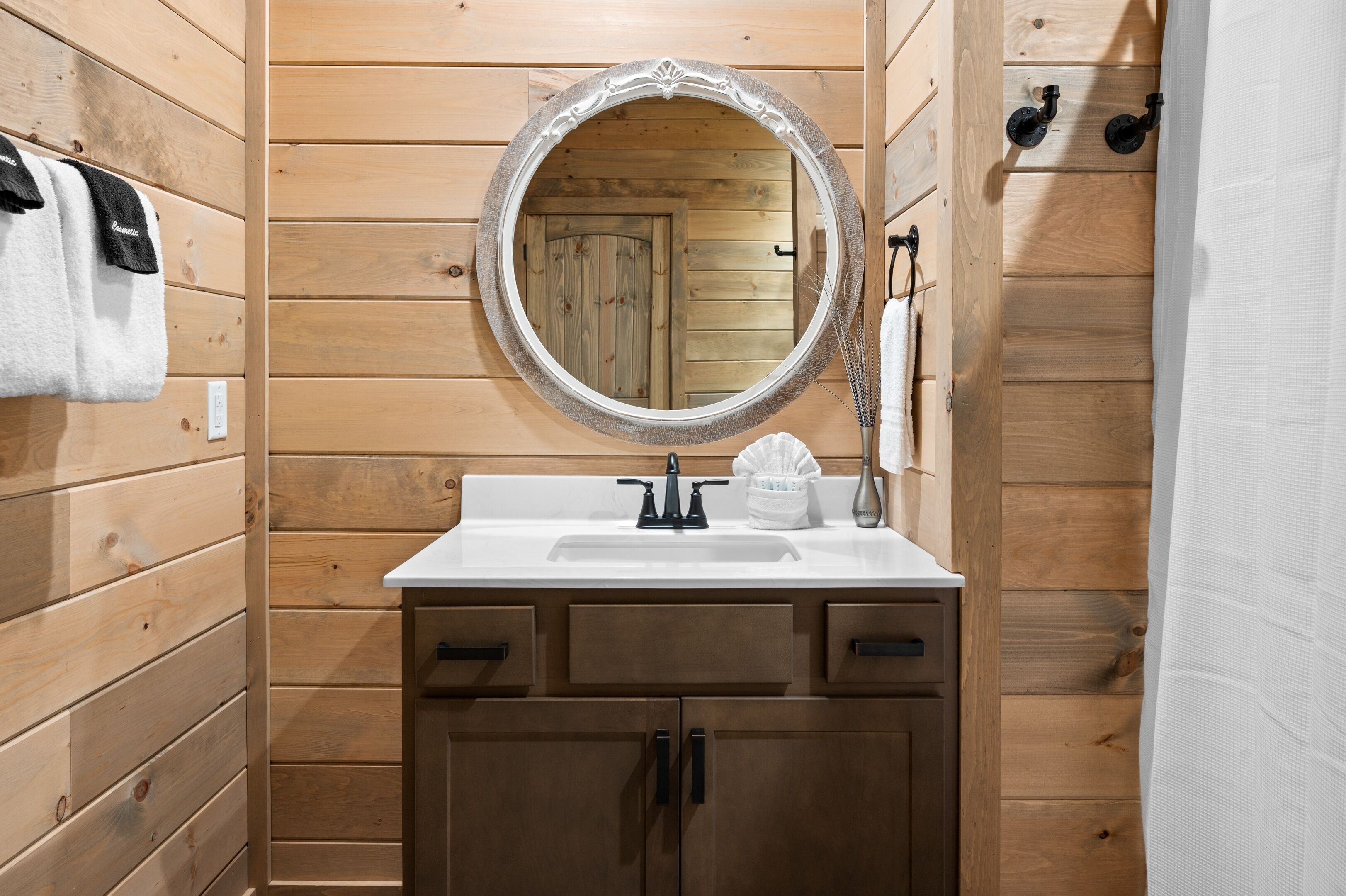 Un baño con paneles de madera, un espejo redondo, un lavamanos blanco y armarios de madera.
