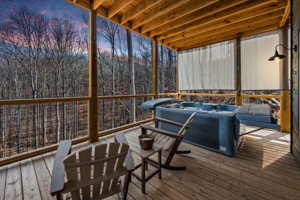 Una terraza de madera con un jacuzzi, sillas Adirondack y vistas a un bosque.