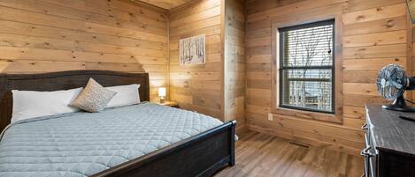 A wooden-paneled bedroom with a bed, a ceiling fan, a window, and a nightstand.