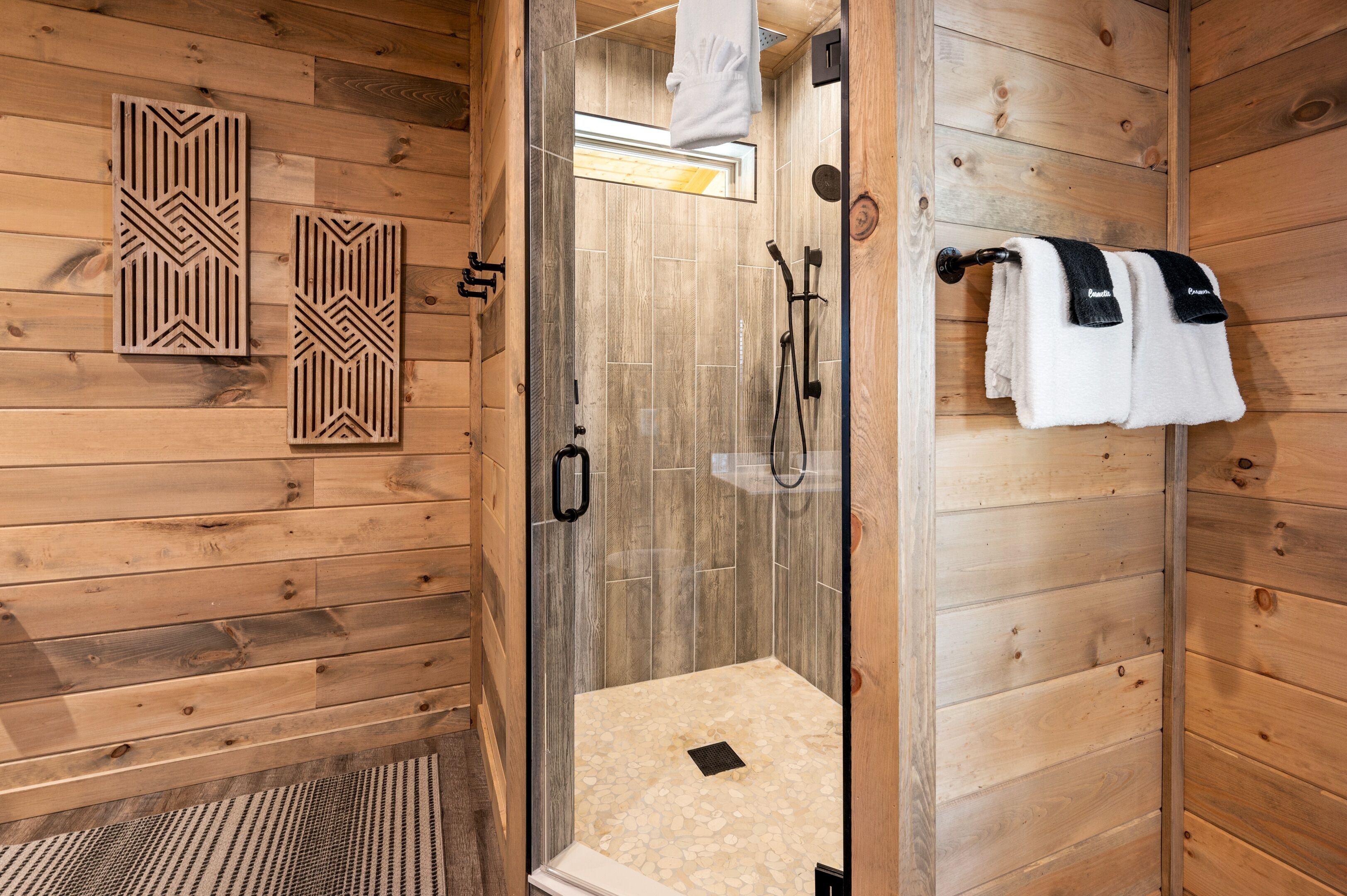 A wooden cabin bathroom with a glass-enclosed shower, wooden walls, and a towel rack with towels.