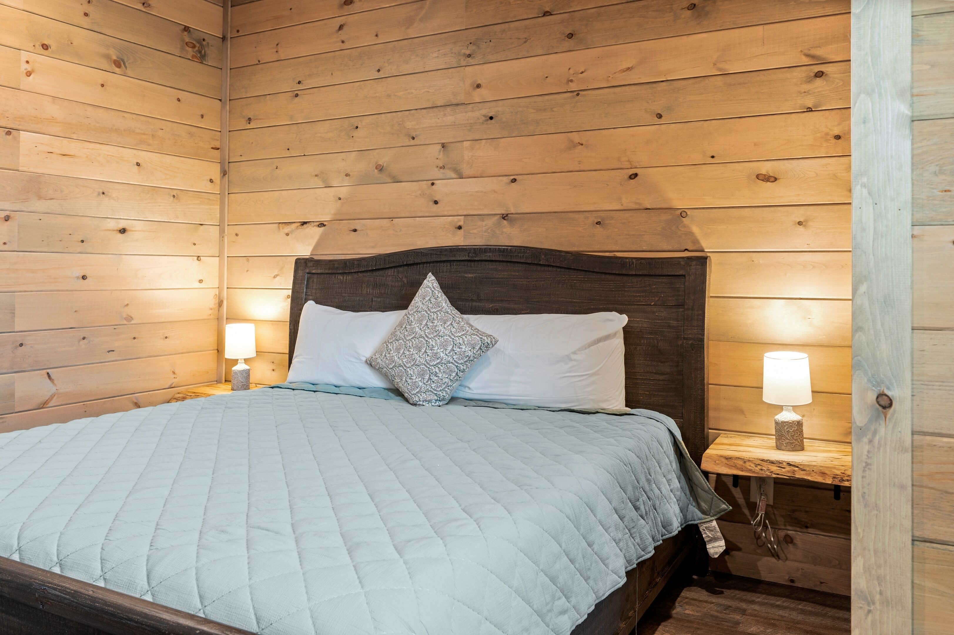 Een kamer met houten lambrisering, een bed, twee bedlampen en een kussen met een patroon.