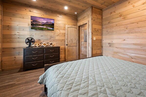 Una habitación con paneles de madera, una cama, un aparador, un ventilador y una puerta.