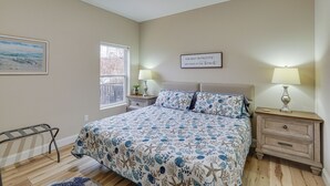 A bedroom with a bed, two bedside tables with lamps, a window, a framed picture, and a wall sign. - Lake Ozark Apartment w/ Balcony < 1 Mi to Water! (Lake Ozark)