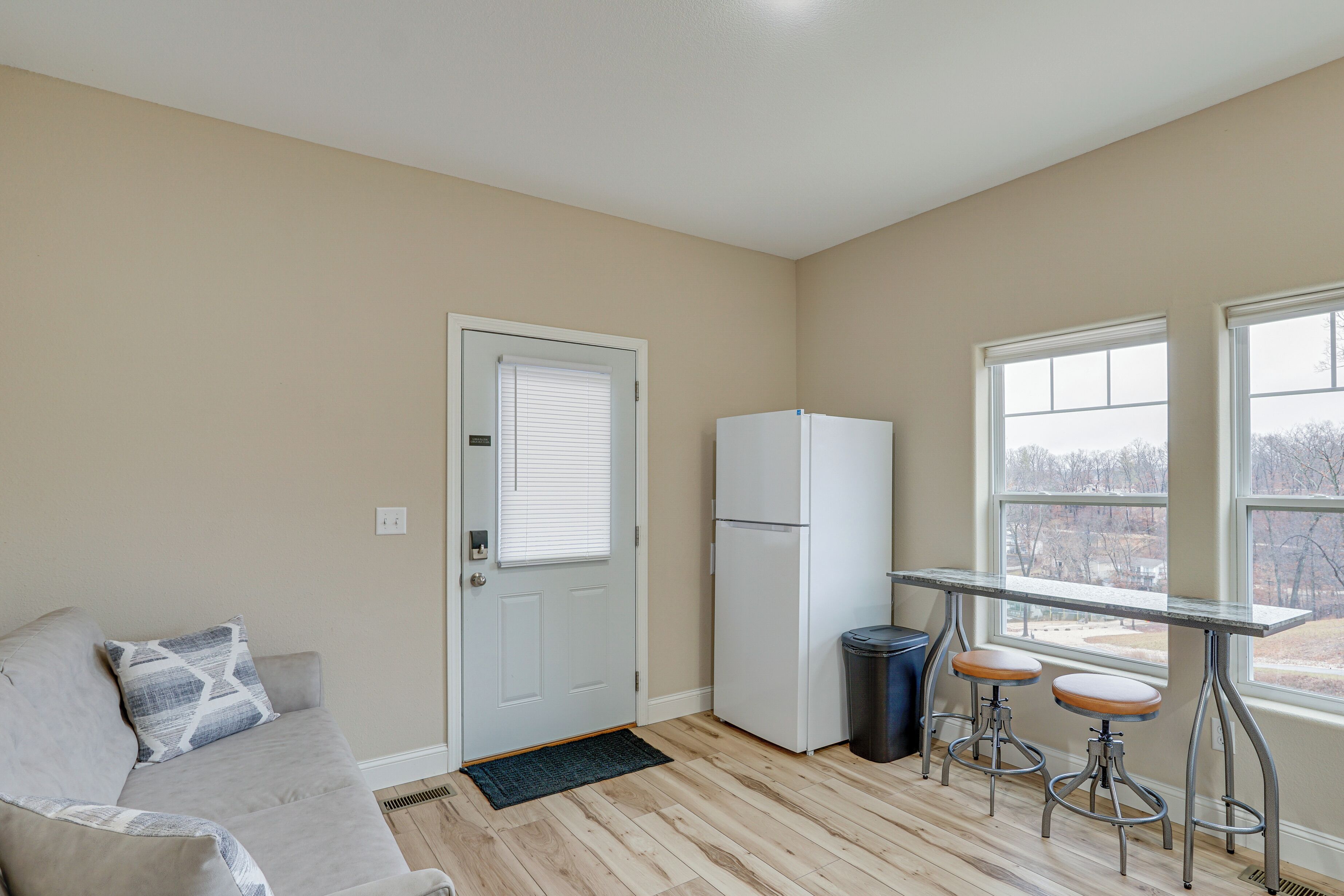 A compact living space with a kitchenette, a door with a window, a sofa, and a small bar area with stools.
