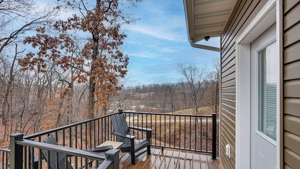 A wooden deck with two chairs and a table, overlooking a forested area. - Lake Ozark Apartment w/ Balcony < 1 Mi to Water! (Lake Ozark)