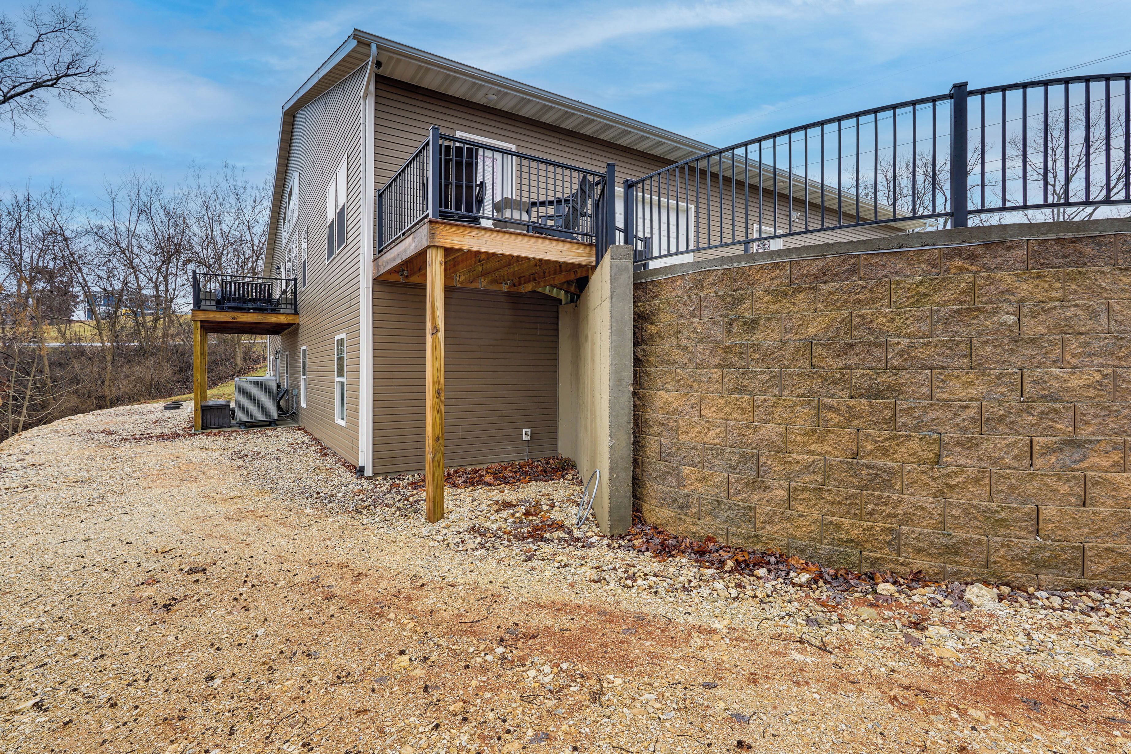 A two-story house with a balcony, a stone wall, and a gravel driveway.