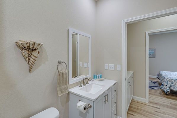 A bathroom with a white sink, mirror, and toilet. There is a towel rack with a towel and a decorative leaf on the wall. - Lake Ozark Apartment w/ Balcony < 1 Mi to Water! (Lake Ozark)