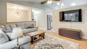 A modern living room with a grey sofa, a wooden coffee table, a patterned rug, a ceiling fan, and a flat-screen TV mounted on the wall. - Pet-friendly Fletcher Home - 13 Mi to Asheville! (Fletcher)