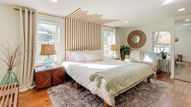 Un dormitorio moderno con una cama grande, cabecera de madera, mesitas de noche con lámparas, un espejo y vistas al exterior.