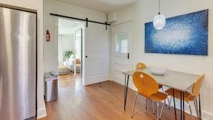 Una cocina moderna con un refrigerador de acero inoxidable, una mesa de comedor con cuatro sillas y un cuadro abstracto grande en la pared.