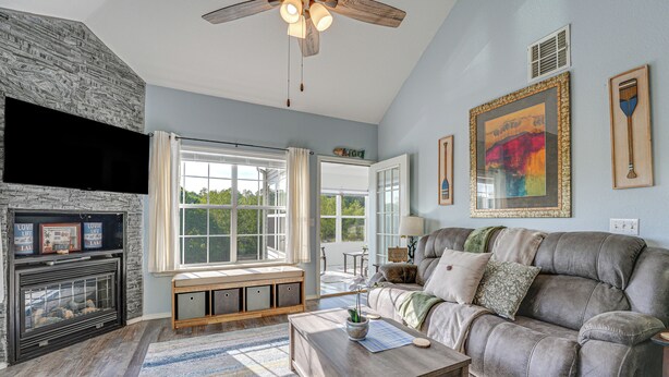 A living room with a fireplace, a large window, a sofa, and a ceiling fan. - Updated Branson Condo w/ Lake Taneycomo Views! (Branson)