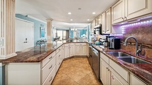 A modern kitchen with white cabinets, granite countertops, stainless steel appliances, and a central island. - Inlet Reef 515 2 Bedroom Condo by RedAwning (Destin)