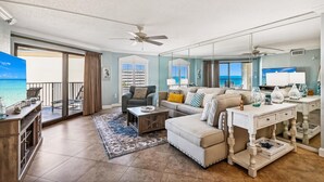 A spacious living room with a large sofa, a coffee table, and a TV. There is a balcony with a view of the ocean. - Inlet Reef 515 2 Bedroom Condo by RedAwning (Destin)