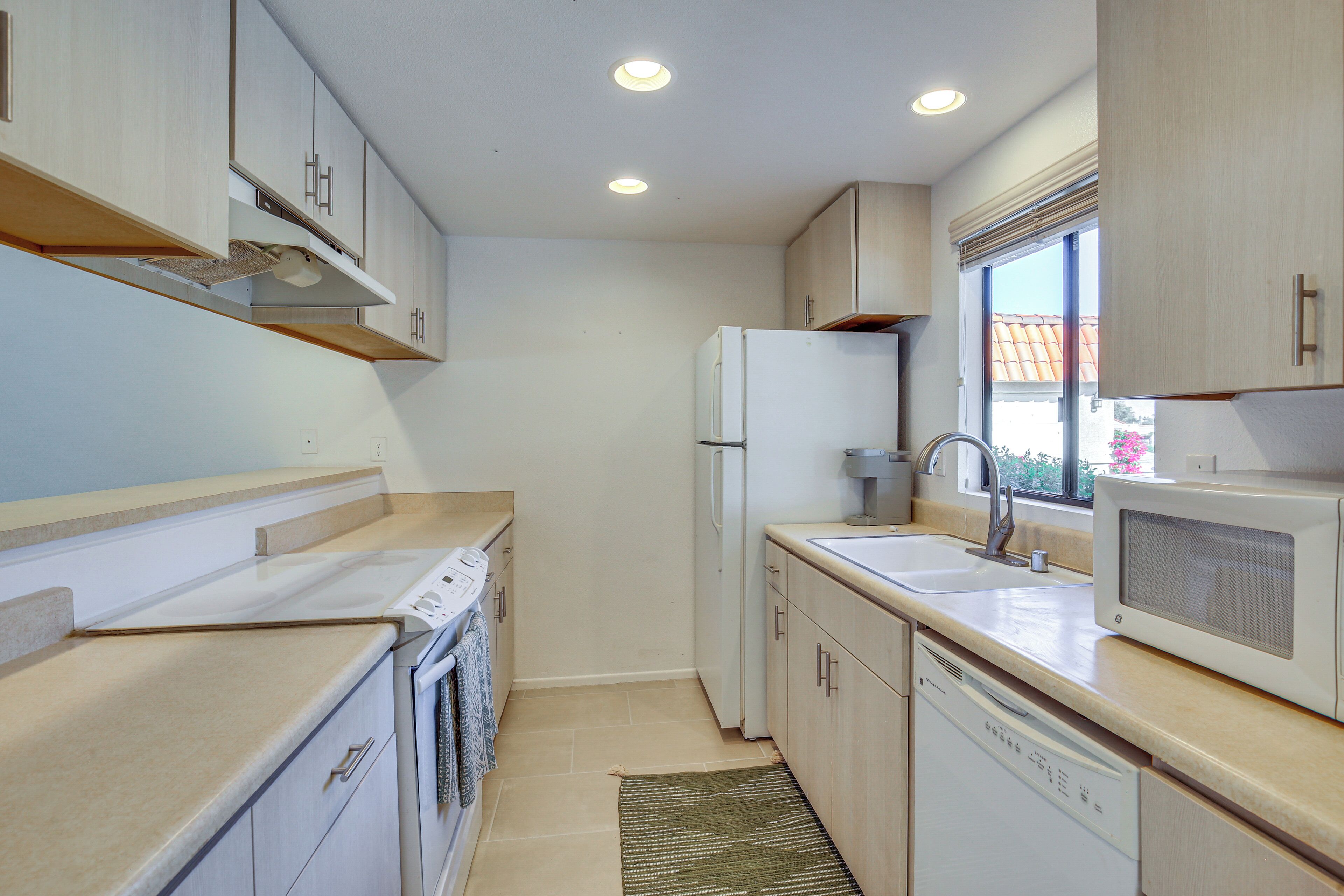 A compact kitchen with a built-in oven, microwave, and dishwasher, wooden cabinets, and a window providing natural light.