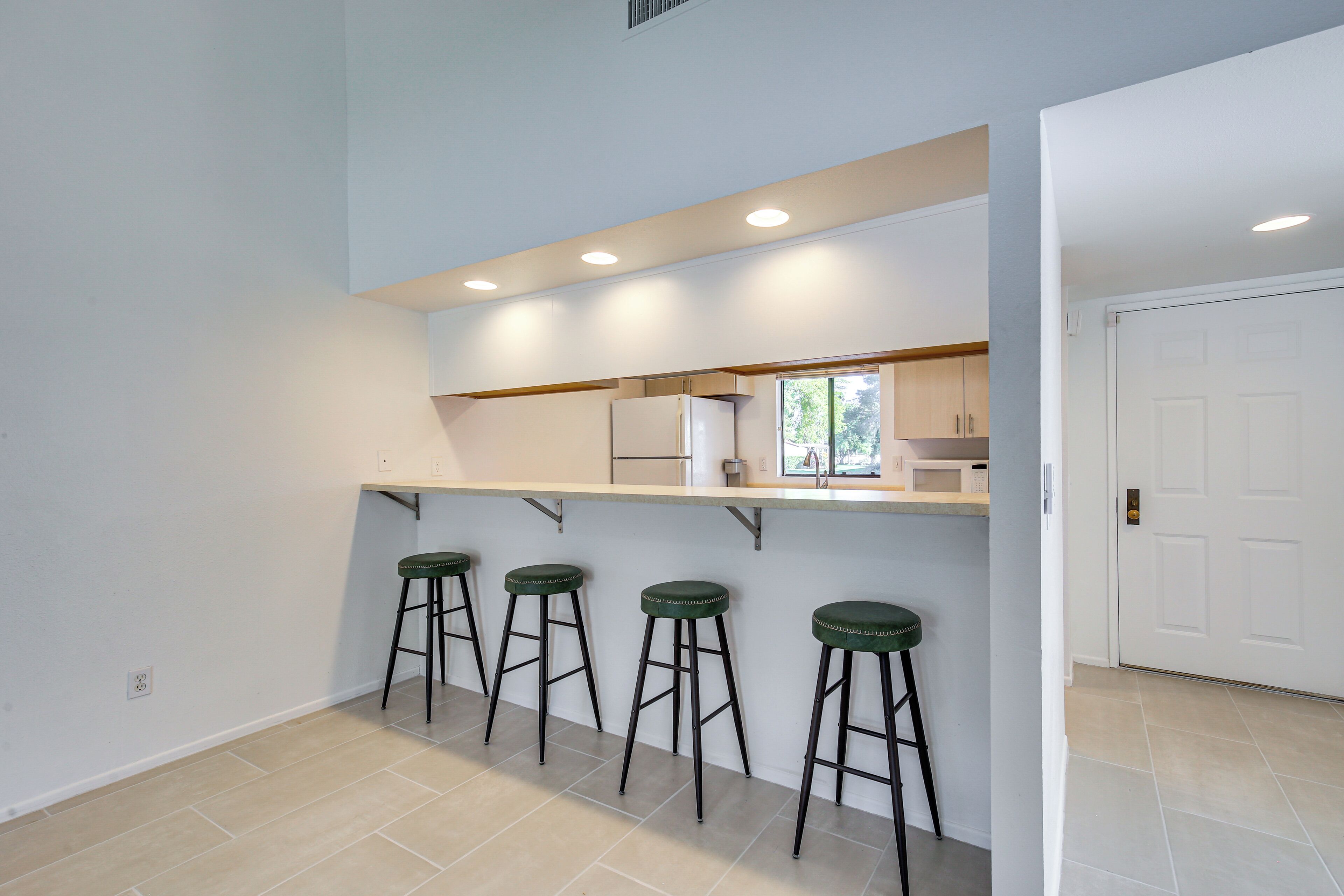 A kitchen with a bar area, three stools, and a white door.